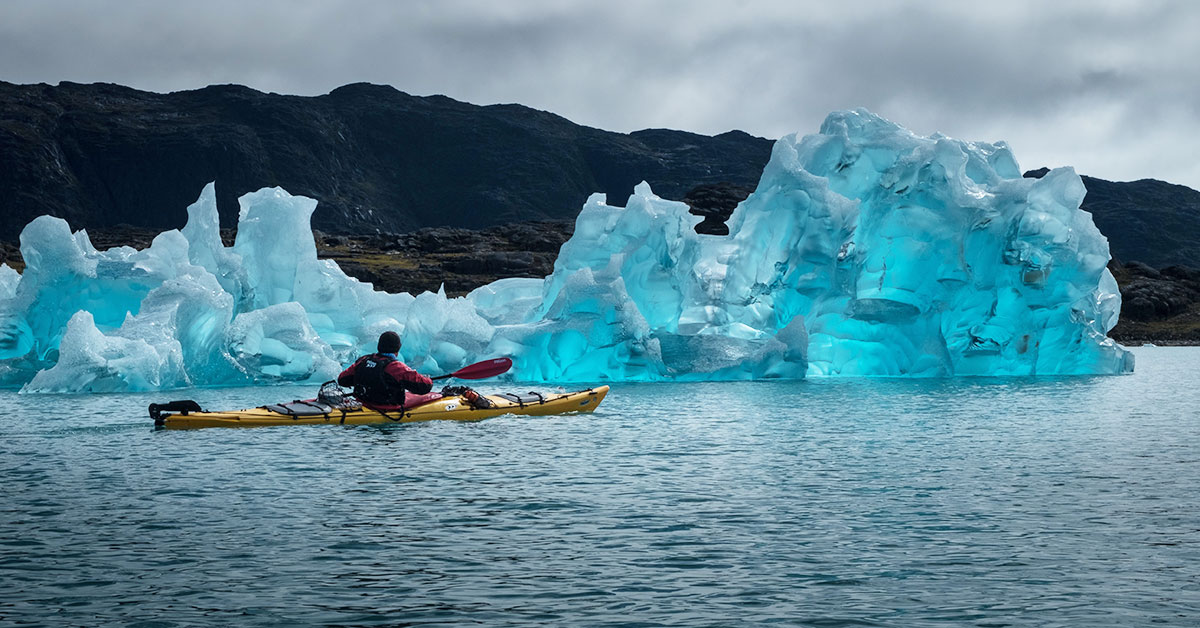 Man in kayak next to iceberg