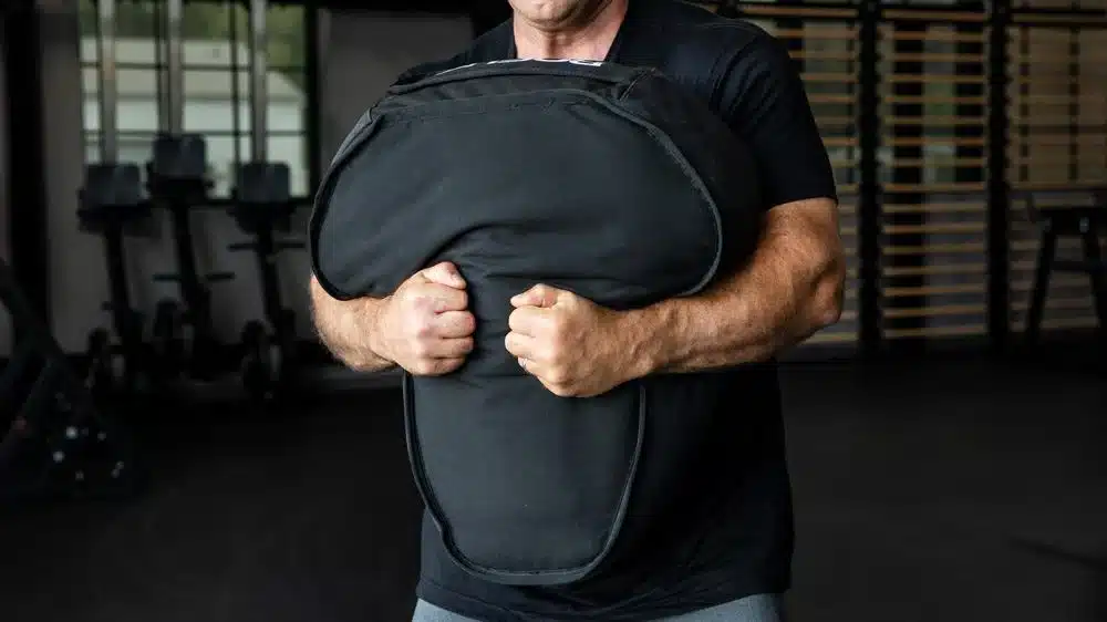 Man training in gym with sandbag.