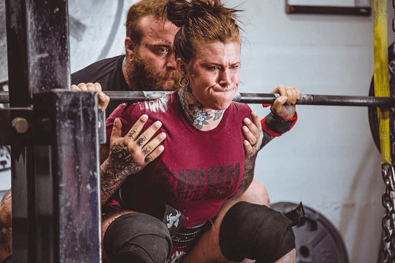 Woman squatting barbell with spotter