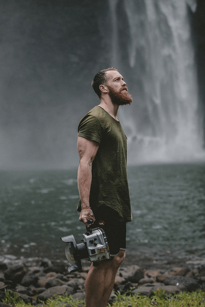 Man carrying camera next to waterfall